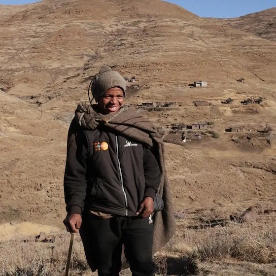  A young man stands against a hilly backdrop.